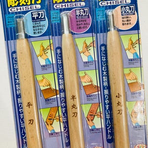 May include: Three wood carving chisels with wooden handles. The chisels are labeled "Flat Head Chisel", "Blow Round Head Chisel", and "Narrow Round Head Chisel". Each chisel has a different shape and size blade. The chisels are packaged in plastic with Japanese text.