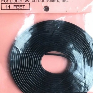 May include: A black 3-wire flat cable, #22 gauge, for Lionel switch controllers, etc. The cable is coiled and packaged in a clear plastic bag with a pink label that reads "3-WIRE FLAT CABLE -- #22 GAUGE" and "For Lionel switch controllers, etc." The label also states "11 FEET".