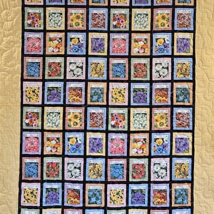 May include: A handmade quilt featuring a repeating pattern of colorful flower seed packets. Each square showcases a different floral arrangement, framed by a gingham border and set against a black background. The quilt has a yellow border.