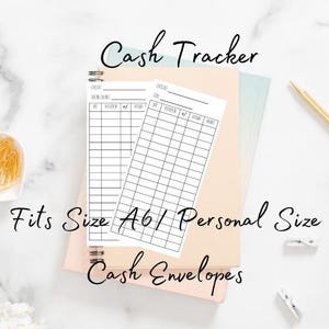 May include: A stack of cash tracker and cash envelope inserts, with the text "Cash Tracker", "Fits Size A6 / Personal Size", and "Cash Envelopes". The inserts are white with black grid lines and text, resting on a spiral-bound notebook.