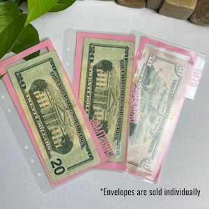 May include: Pink and clear plastic envelopes holding U.S. currency. The bills are twenty and fifty dollar denominations. The envelopes have a pink border and are designed to fit into a binder. The text "AMERICA" is printed on the envelopes.