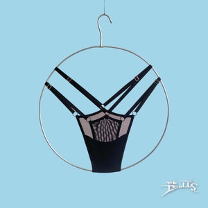 May include: Black thong underwear featuring a sheer mesh panel at the front, multiple adjustable elastic straps with silver-toned metal rings and sliders, all suspended from a circular metal hanger against a light blue background.