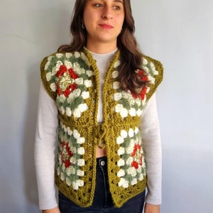 May include: A green, white, and red crocheted vest with a square pattern. The vest has a tie closure at the front.