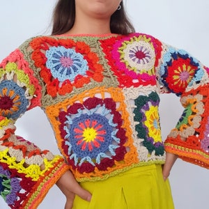 May include: A colorful crochet top with a square pattern and long sleeves. The top is made of different colored yarn, including red, orange, yellow, green, blue, and purple.