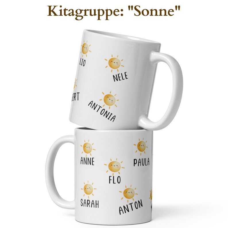 May include: Two white ceramic mugs stacked on top of each other. Each mug features a repeating pattern of smiling sun illustrations and names. The text "Kitagruppe: Sonne" is at the top. The mugs have a handle on the side.