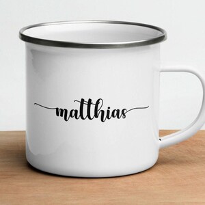 Può includere: Tazza in smalto bianco con bordo argentato e il nome "matthias" scritto in corsivo nero.