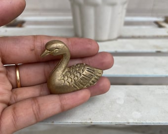 Könnte beinhalten: Eine kleine, goldfarbene Schwanenfigur aus Messing. Der Schwan ist in Schwimmhaltung dargestellt, mit dem Kopf zur Seite gedreht.