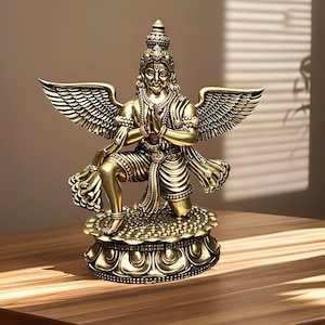 May include: A gold-coloured statue of a deity with large wings, kneeling with hands in prayer. The statue is highly detailed, with intricate carvings and ornamentation. It is mounted on a decorative base, and the overall effect is one of reverence and artistry.