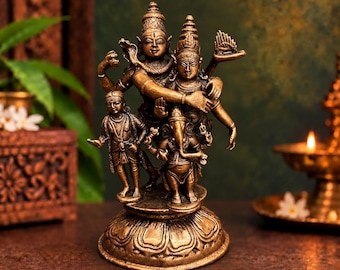 May include: A bronze-toned metal statue depicting a group of four figures standing on a circular lotus-shaped base. The central figures include a deity with multiple arms embracing another, accompanied by a smaller standing figure and Ganesha.
