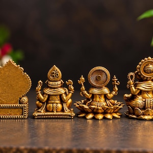 May include: Four gold-colored statues arranged in a row. The first is a rectangular plaque with a pointed top. The second is a deity figure with an Om symbol. The third is a deity on a lotus base. The fourth is a deity with a circular halo.