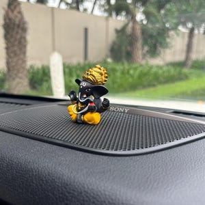 Puede incluir: Una peque&ntilde;a figura negra y dorada de Ganesha, el dios hind&uacute; de la sabidur&iacute;a y la prosperidad, sentada en el tablero de instrumentos de un coche negro con un logotipo de SONY.