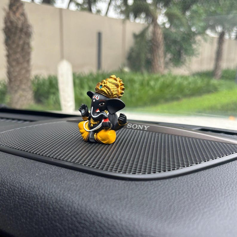 Puede incluir: Una peque&ntilde;a figura negra y dorada de Ganesha, el dios hind&uacute; de la sabidur&iacute;a y la prosperidad, sentada en el tablero de instrumentos de un coche negro con un logotipo de SONY.