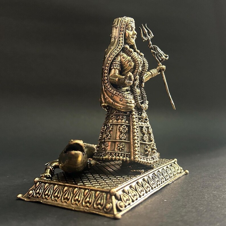 K&ouml;nnte beinhalten: Bronzefarbene Statue einer Gottheit, die einen Dreizack h&auml;lt. Die Figur ist mit aufwendigen Details geschm&uuml;ckt, darunter verzierte Kleidung und Schmuck. Am Sockel der Statue, die auf einem dekorativen Sockel steht, befindet sich eine Krokodilfigur.