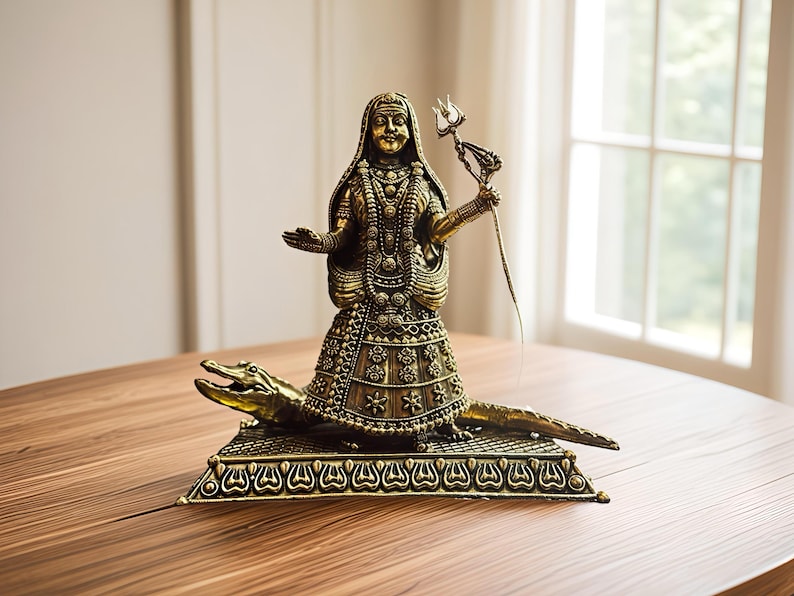K&ouml;nnte beinhalten: Eine detaillierte Bronzestatue einer Gottheit, geschm&uuml;ckt mit aufwendigem Schmuck und Kopfschmuck, die einen Dreizack h&auml;lt. Die Figur steht auf einem Krokodil, das auf einem dekorativen Sockel montiert ist. Die Statue steht auf einem Holztisch.