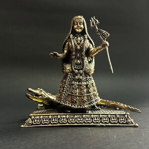 K&ouml;nnte beinhalten: Eine bronzefarbene Statue einer Gottheit, verziert mit komplizierten Details, steht auf einem Krokodilsockel. Die Figur h&auml;lt einen Dreizack und ist mit aufwendiger Kleidung bedeckt. Die Statue steht vor einem dunklen Hintergrund, der ihre Handwerkskunst hervorhebt.