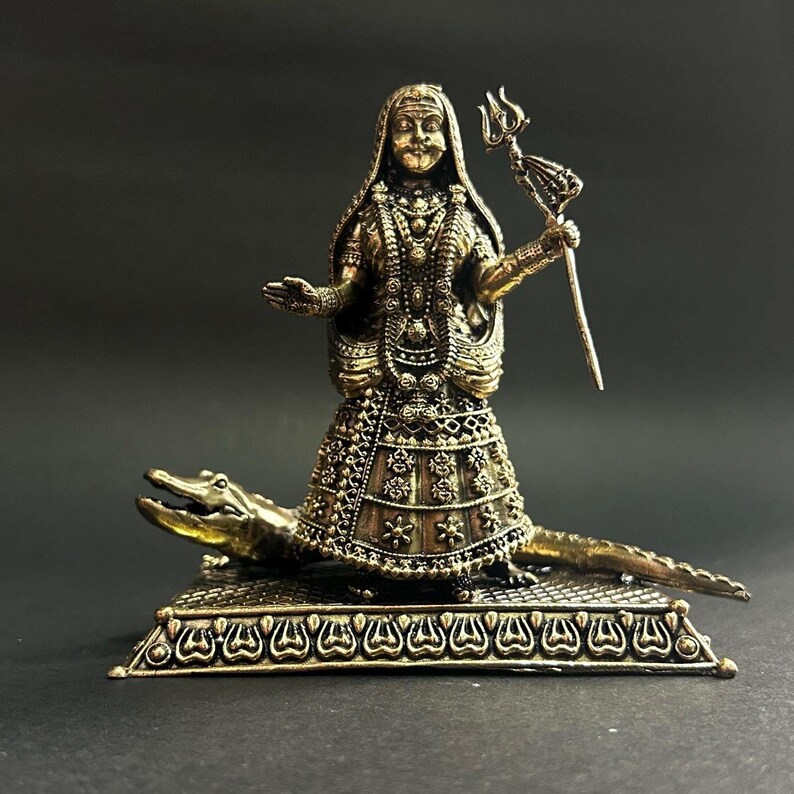 K&ouml;nnte beinhalten: Eine bronzefarbene Statue einer Gottheit, verziert mit komplizierten Details, steht auf einem Krokodilsockel. Die Figur h&auml;lt einen Dreizack und ist mit aufwendiger Kleidung bedeckt. Die Statue steht vor einem dunklen Hintergrund, der ihre Handwerkskunst hervorhebt.
