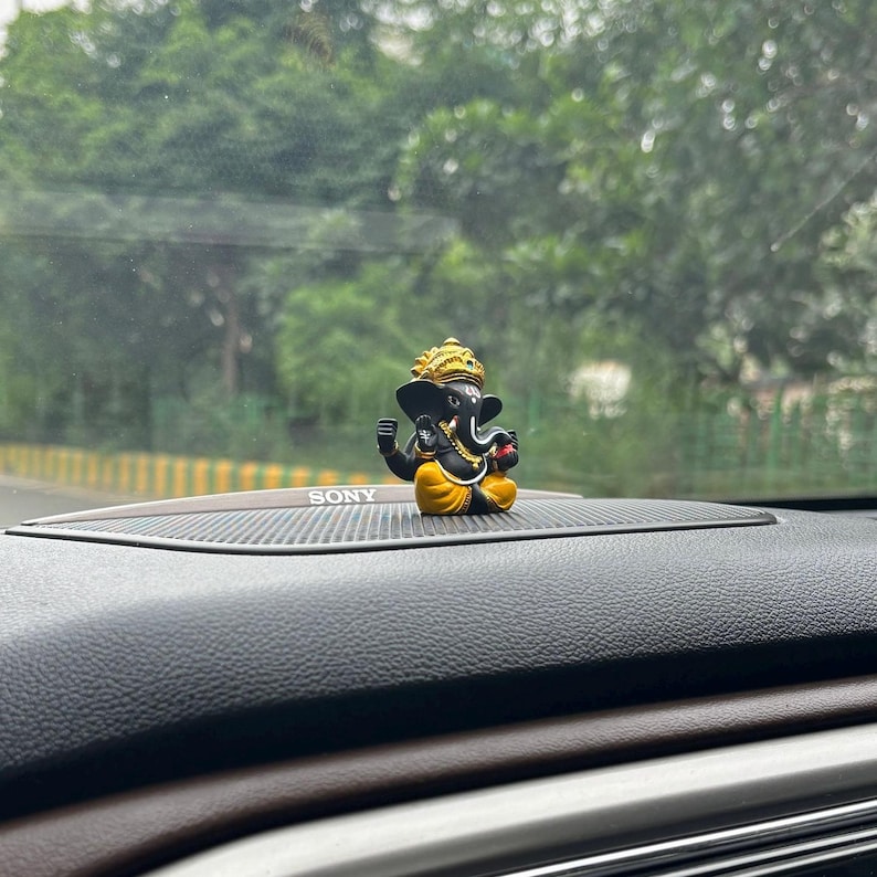 Puede incluir: Una peque&ntilde;a figura negra y dorada del dios hind&uacute; Ganesha, sentada en el tablero de un coche con la palabra "SONY" visible.