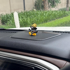 Puede incluir: Una peque&ntilde;a figura negra y dorada del dios hind&uacute; Ganesha, sentado en una postura meditativa. La figura est&aacute; colocada en el tablero de un coche, delante de un altavoz negro con la etiqueta "SONY".