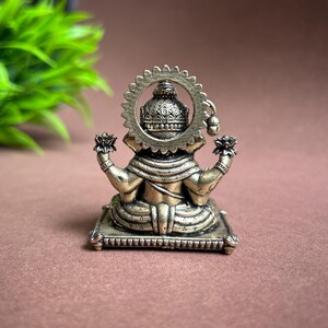 May include: A gold-colored metal statue of Ganesha, the Hindu god of wisdom and prosperity, sitting on a decorative base. The statue is detailed with intricate carvings and features a halo behind the head.