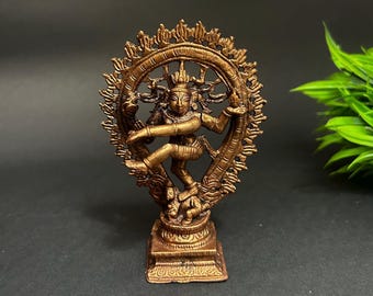 May include: A bronze-colored statue of a dancing figure within a circular frame. The figure is posed dynamically, with one leg raised and arms outstretched. The statue is on a square base and set against a dark background.