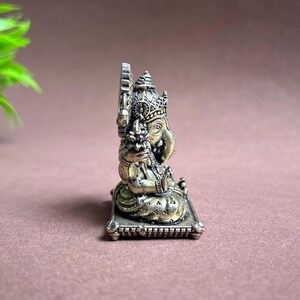 May include: A gold-colored metal statue of Ganesha, the Hindu god of wisdom and prosperity, sitting on a decorative base. The statue is intricately detailed and features a traditional design.