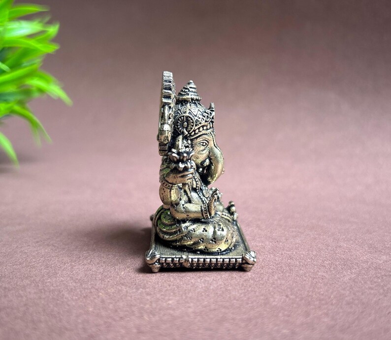 May include: A gold-colored metal statue of Ganesha, the Hindu god of wisdom and prosperity, sitting on a decorative base. The statue is intricately detailed and features a traditional design.