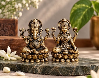 Peut inclure: Deux statues en métal doré représentant des divinités assises sur des socles en forme de lotus. La figure de gauche a une tête d'éléphant et plusieurs bras, tandis que celle de droite est une divinité humaine tenant des lotus.