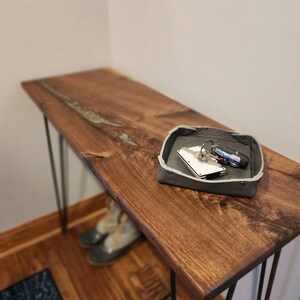 May include: A dark brown wooden console table with black hairpin legs. A small gray tray with keys and a wallet sits on the table.