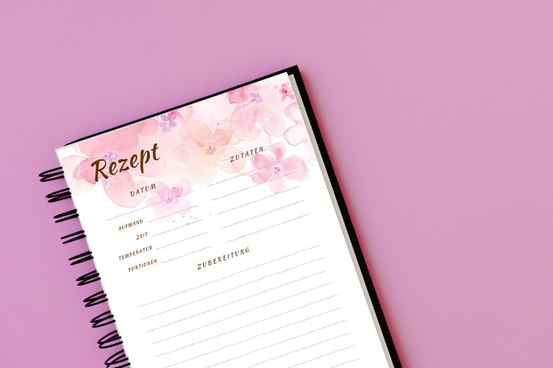 May include: A white recipe journal with a black spiral binding. The cover features a watercolour design of pink and peach flowers. The journal has sections for the recipe name, date, ingredients, and preparation instructions.
