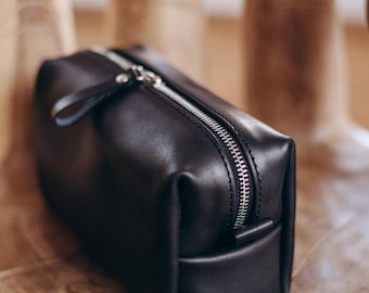 May include: A black leather zippered travel toiletry bag with a silver zipper.