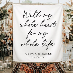 Pode incluir: Um pano de fundo de tecido branco com a escrita preta que diz: "With my whole heart for my whole life". Abaixo do texto est&atilde;o os nomes "OLIVIA & JAMES" e a data "24.06.21". O pano de fundo faz parte de uma cerim&oacute;nia de casamento.