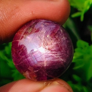 May include: A round, red ruby gemstone with a star-like pattern and a shiny, iridescent finish.