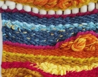 Puede incluir: Un tapiz tejido de pared colorido con una rama de madera en la parte superior y una franja de hilo en la parte inferior. El tapiz presenta una variedad de colores, incluyendo rojo, naranja, amarillo, azul y blanco.