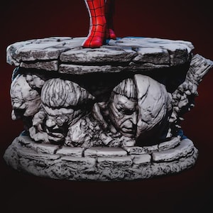 May include: A detailed statue base featuring sculpted villain faces in shades of gray. The base supports a figure with red boots. The base has a textured, stone-like appearance, with a dark red background.