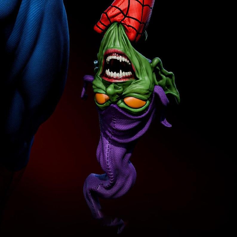 May include: A detailed sculpture of the Green Goblin's head, held upside down by a red and black gloved hand. The Goblin has green skin, orange eyes, and a purple cowl. The background is dark.