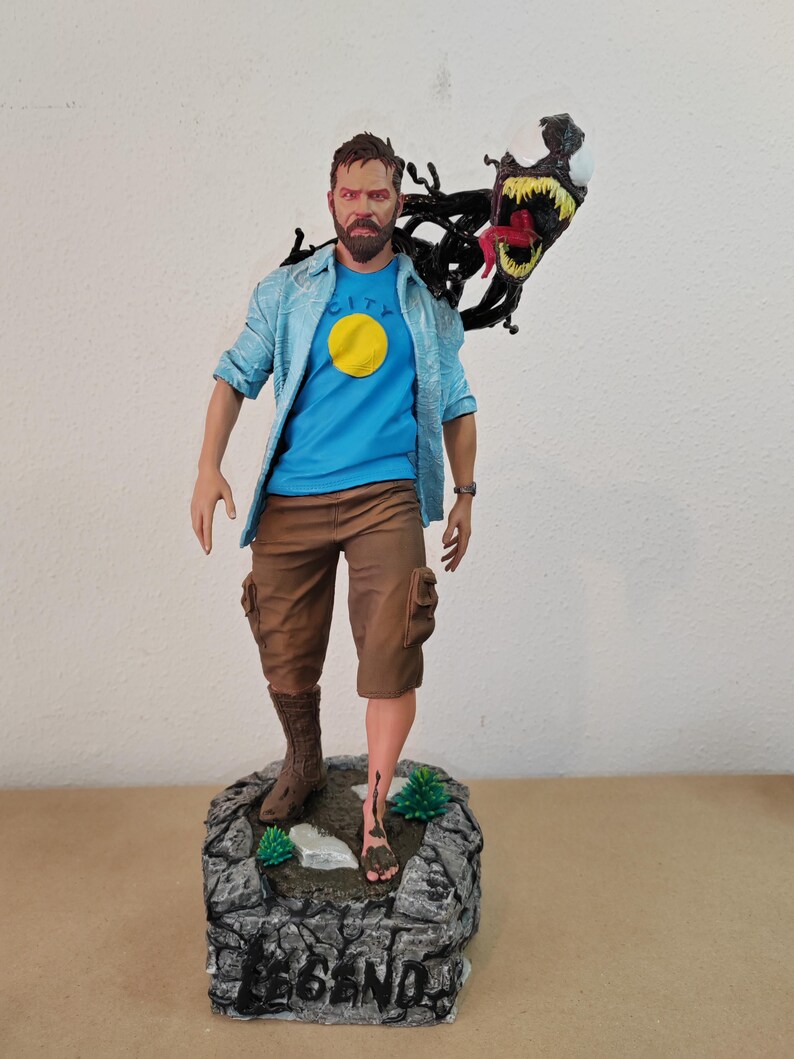 以下が含まれることがあります： ひげを生やした男性のフィギュアで、青いシャツに黄色の円、茶色のショートパンツを着用しています。口の大きな黒と赤の生き物が背後から現れています。フィギュアは、灰色の岩の台座の上に立っており、台座には「LEGEND」と書かれています。