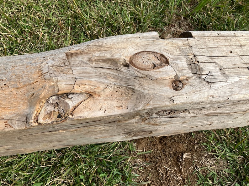 May include: Close-up of a weathered wooden beam with several knots and a rough texture. The beam is light brown in color and has a natural, rustic look.