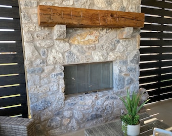May include: A stone fireplace with a wooden mantel and a black metal screen door. The fireplace is surrounded by a stone wall and is located in an outdoor patio area.