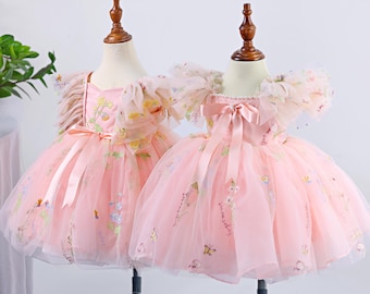 May include: Two pink tulle dresses with floral embroidery and ruffled sleeves. The dresses have a satin ribbon tied at the waist.