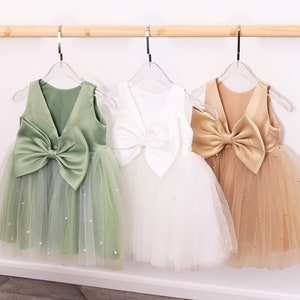 May include: Three tulle dresses with satin bows on the back. The dresses are green, white, and gold.
