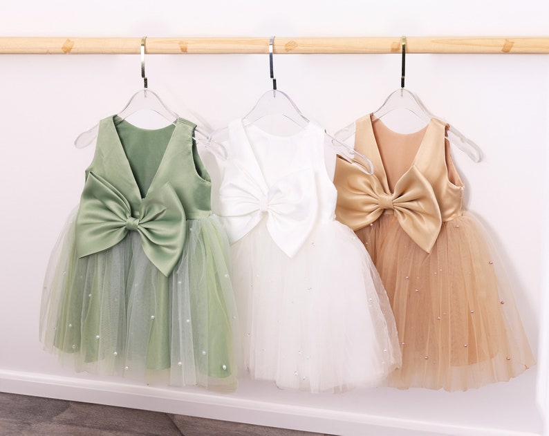 May include: Three tulle dresses with satin bows on the back. The dresses are green, white, and gold.