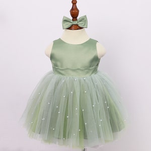May include: A sage green tulle dress with a satin bodice and pearl embellishments. The dress has a bow on the top.