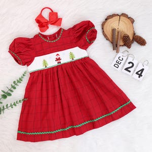 Può includere: Abito rosso a quadri con un giogo ricamato bianco con un Babbo Natale e alberi di Natale. L'abito ha bordi verdi e maniche a sbuffo.