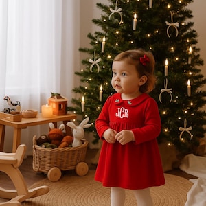 Può includere: Una bambina con un vestito rosso, calzamaglia bianca e scarpe rosse è in piedi davanti a un albero di Natale decorato. L'abito ha un colletto bianco con dettagli ricamati e le iniziali "JCR". Un cesto di vimini con giocattoli e un cavallo a dondolo in legno sono nelle vicinanze.