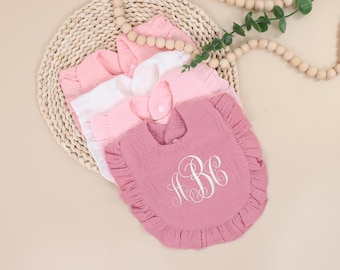 May include: A set of four pink and white baby bibs with ruffled edges. The bibs are made of soft cotton and feature embroidered monograms. The bibs are stacked on top of each other, with the top bib featuring the monogram "A.B.C."