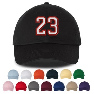 Puede incluir: Una gorra de béisbol negra con el número 23 bordado en rojo y blanco en la parte delantera. La gorra está disponible en una variedad de colores.