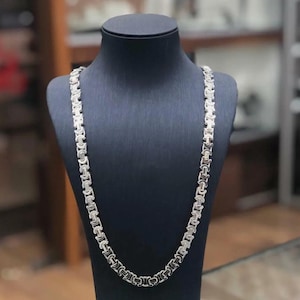 May include: A silver chain necklace with a box link design. The necklace is displayed on a black mannequin bust.