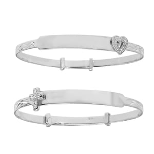 May include: Two silver baby bangles with a blank space for engraving. One bangle has a heart charm with small clear stones and the other has a cross charm with small clear stones.
