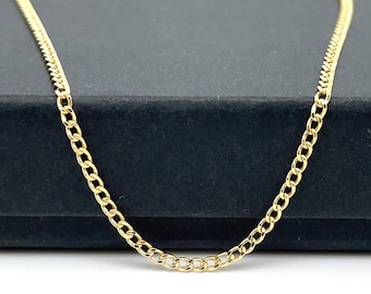 May include: A gold chain necklace with a curb link style. The chain is laying on a black surface.