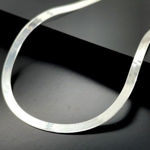 May include: A silver snake chain necklace with a polished finish. The chain is flat and has a subtle herringbone pattern.